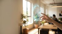 Hand touching glowing digital hologram interface in modern office workspace with natural light and blurred colleagues in background for technology and innovation concepts.
