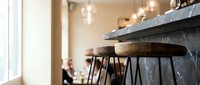 Wooden bar stools with black metal frames positioned at a rustic counter, pendant lights hanging above, warm interior design for restaurant, cafe, or home bar decor.