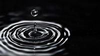 Single water drop falling into dark liquid creating concentric ripples, captured in dramatic black and white with high contrast for environmental or wellness concepts.