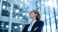 Young Asian businesswoman in glasses and suit looking up at digital network visualization floating in modern office space. Technology concept.