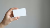 Person of indeterminate ethnicity holding blank white business card or mockup template against neutral gray background for branding and corporate identity projects.