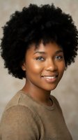 Young African American woman with natural curly afro hair smiling warmly in brown sweater against neutral background for lifestyle and portrait photography.
