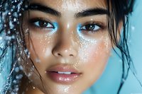 Close up portrait of young Asian woman with wet glowing skin, glitter makeup, and water drops against turquoise background, beauty and cosmetics concept.
