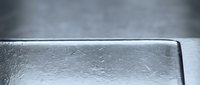 Clear ice block with textured surface and smooth edges against gray background for cooling, preservation, and beverage applications in commercial settings.