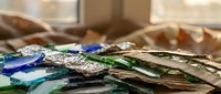 Colorful stained glass pieces scattered on wooden surface in bright workshop interior for artistic crafts and creative projects.