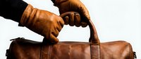 Two hands in brown leather gloves gripping a vintage leather travel bag, symbolizing journey, adventure, and timeless craftsmanship for travel and lifestyle content.