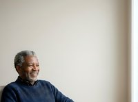 Senior man with gray hair and beard, African descent, wearing dark blue sweater, smiling while looking to the side against neutral wall background for portrait and lifestyle use.