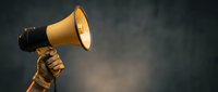 Hand holding vintage yellow megaphone against dark background for communication, announcement, marketing campaigns and promotional materials.
