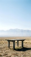 Weathered wooden table sits alone in vast desert landscape with distant mountains under clear sky, evoking solitude and abandonment for conceptual and editorial projects.