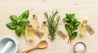 Natural essential oil bottles with fresh herbs basil rosemary mint on wooden background. Organic aromatherapy spa wellness concept with mortar pestle spoon salt.