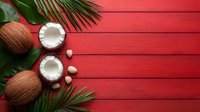 Fresh coconuts split in half with palm leaves arranged on vibrant red wooden planks background, creating tropical summer composition with copy space.