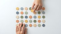 Hand arranging colorful wooden emotion tokens in organized grid pattern for mindfulness therapy and emotional wellness activities on white surface.