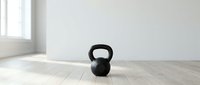 Black kettlebell weight on wooden floor in bright minimalist gym studio space, suitable for fitness, workout, and health-related design projects.