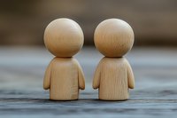 Two minimalist wooden figurines with round heads standing side by side on rustic wooden surface, symbolizing partnership, friendship, or relationship concept.