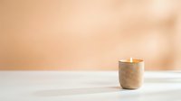 Minimalist wooden candle holder with burning flame on white surface against warm beige background for home decor and relaxation concepts.