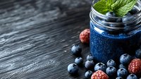 Fresh blue spirulina smoothie garnished with mint leaves, blueberries and raspberries in mason jar on dark wooden background, healthy breakfast concept.