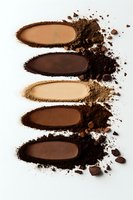 Crushed makeup powder swatches in various brown and nude shades arranged vertically on white background, showing texture and pigment intensity for cosmetic presentation.