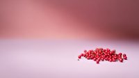 Pink peppercorns scattered on pink surface with soft gradient background creating minimalist culinary composition for food styling and design.