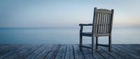 Empty wooden chair on pier overlooking calm ocean at dawn, conveying solitude, contemplation, and peaceful retreat for wellness and lifestyle concepts.