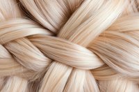 Macro view of light blonde braided hair texture showing intricate weaving pattern and silky smooth strands in warm beige and platinum tones.