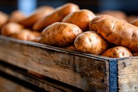 Fresh organic sweet potatoes in rustic wooden crate at farmers market, close up view with selective focus showing natural texture and warm tones.