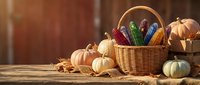 Autumn harvest basket filled with colorful corn cobs surrounded by pumpkins and gourds on rustic wooden table for seasonal decoration and thanksgiving celebration.