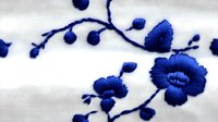 Delicate blue floral embroidery pattern on white fabric with curving stems and blooming flowers creates elegant decorative textile design for fashion and home decor.