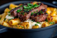 Grilled medium rare beef medallions served on rigatoni pasta with creamy white sauce and fresh herbs, close-up view on dark plate with selective focus.
