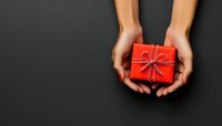 Female hands holding small red gift box with ribbon bow against dark background, copy space for holiday message or seasonal greeting card design.