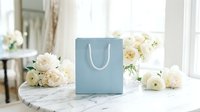 Luxury shopping bag with white rope handles surrounded by fresh cream roses on marble table, suitable for retail, fashion, and gift packaging concepts.