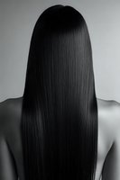 Back view of Asian woman with long straight black hair against gray background, showcasing healthy, sleek hairstyle in monochrome photography.