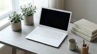 Laptop with blank screen on white desk with potted plants, coffee mug, books and office supplies in bright workspace for remote work, business and productivity projects.