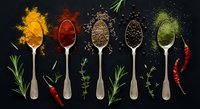 Colorful spices and herbs arranged on wooden spoons against dark background. Turmeric, paprika, seeds and green powder with fresh herbs and chili peppers.