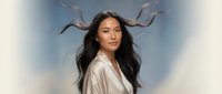 Young Asian woman with flowing dark hair in white shirt against dreamy sky background with soft clouds and ethereal lighting for wellness and beauty concepts.