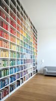 Modern home library with floor-to-ceiling white bookshelves filled with colorful books arranged by color spectrum creating rainbow effect in reading room.