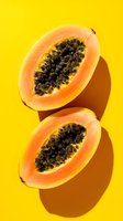 Fresh papaya halves with black seeds on vibrant yellow background, casting dramatic shadows. Great for tropical food marketing.