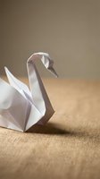 White paper origami swan on natural burlap fabric background with soft lighting for craft and art projects.
