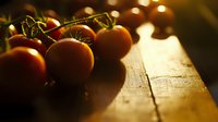 Fresh ripe cherry tomatoes on rustic wooden surface in warm golden sunlight, shallow depth of field creates dreamy atmosphere for food photography.