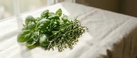 Fresh basil and thyme herbs on white linen cloth for cooking, seasoning, and culinary preparations in natural kitchen setting.