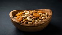 Mixed nuts and dried fruits in rustic wooden bowl on dark background for healthy snacking and cooking ingredients.