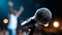 Close-up of professional microphone on stage with blurred performer silhouette in background against colorful stage lights for music concert or event.