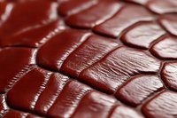 Macro shot of burgundy crocodile leather texture showing detailed scales pattern and surface grain. Luxury material background for fashion design.