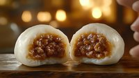 Two steamed buns with savory meat filling cut in half, displayed on wooden surface with warm bokeh lighting, suitable for food photography and culinary content.
