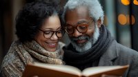 Senior African American couple sharing intimate moment while reading book together, wearing warm scarves and glasses, with soft bokeh lights in background.