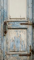 Weathered vintage wooden door with peeling blue and white paint showing rustic charm and aged patina texture for restoration projects.