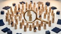 Magnifying glass focusing on wooden figure among crowd of people, talent recruitment and human resources selection concept for business hiring.