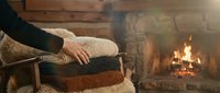Person holding stack of cozy knit sweaters near fireplace with warm flames, perfect for autumn fashion, winter clothing, and seasonal lifestyle content.