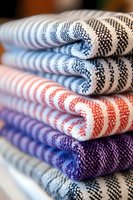 Stack of colorful striped cotton kitchen towels in blue, red, purple, and white patterns, folded neatly for home textile display.