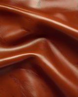 Smooth brown leather texture with soft folds and creases creating elegant waves and shadows, suitable for luxury product backgrounds and fashion design projects.