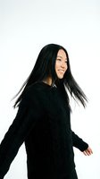 Young Asian woman with long black hair dancing in cozy dark sweater against white background. Joyful movement and genuine smile for lifestyle content.